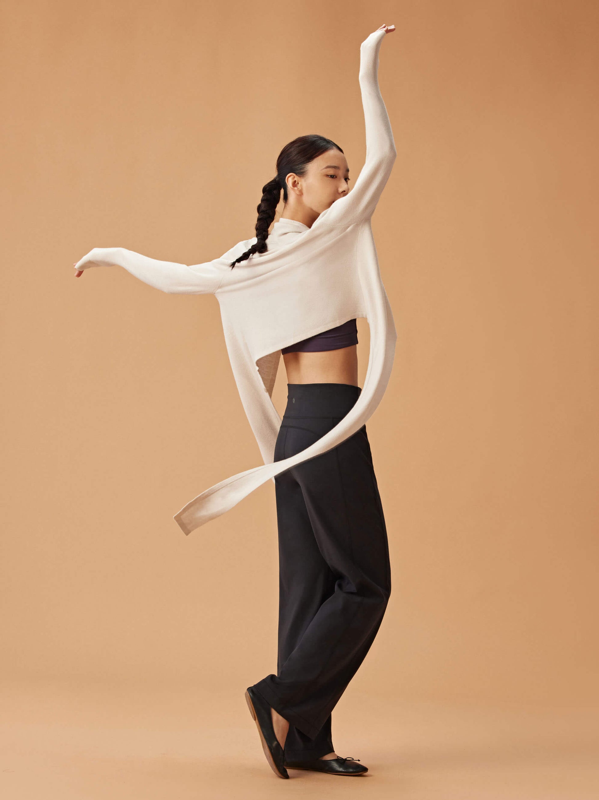 back of woman in white cardigan, dark purple sports bra and black wide leg pants