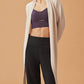 woman in white cardigan, dark purple sports bra and black wide leg pants