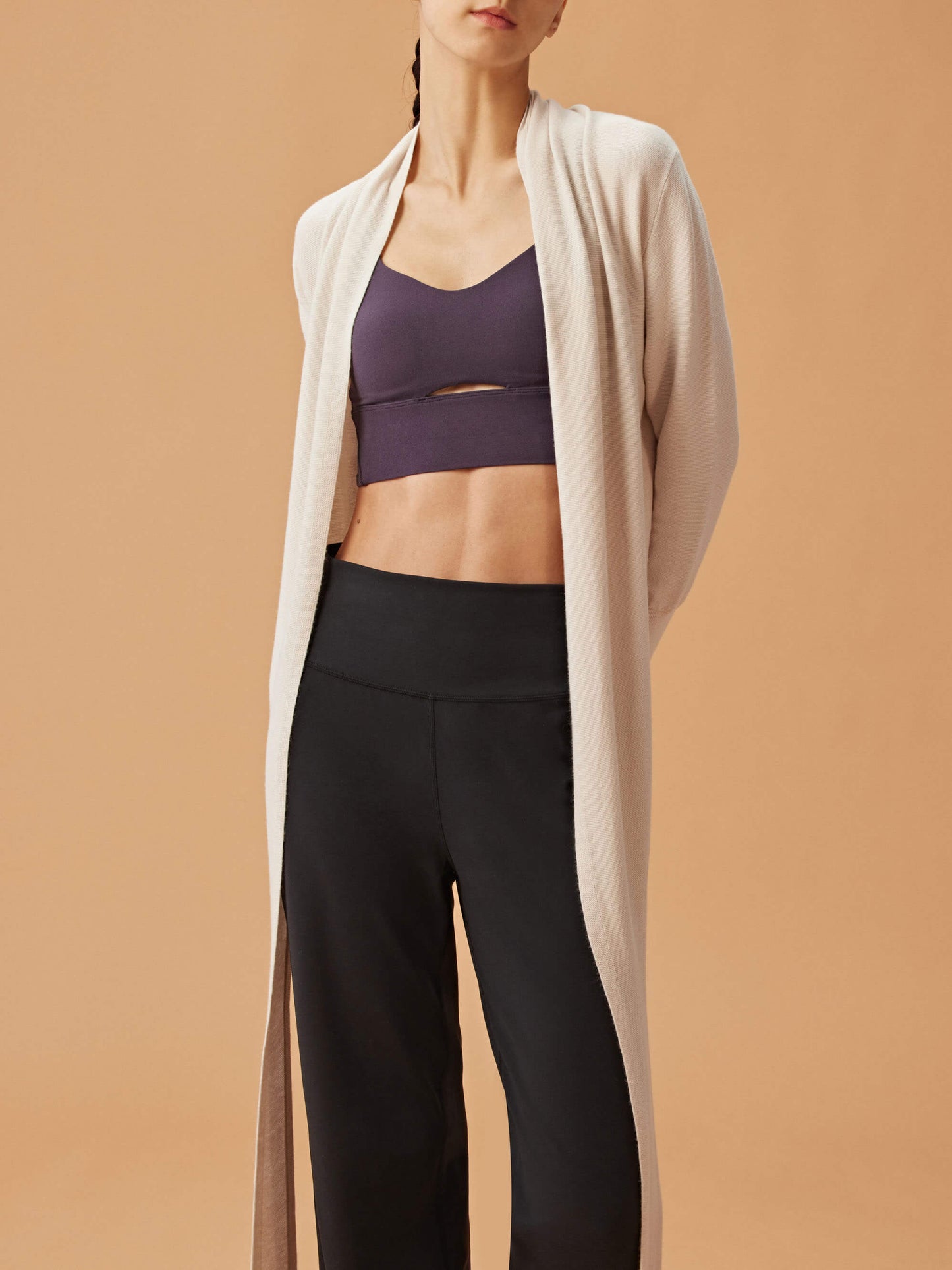 woman in white cardigan, dark purple sports bra and black wide leg pants