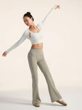Model in a white top and beige pants posing against a plain background