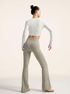 Back view of model wearing a white long-sleeve top and beige flared pants on a plain background