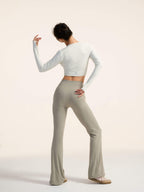 Back view of model wearing a white long-sleeve top and light gray flared pants on a plain background