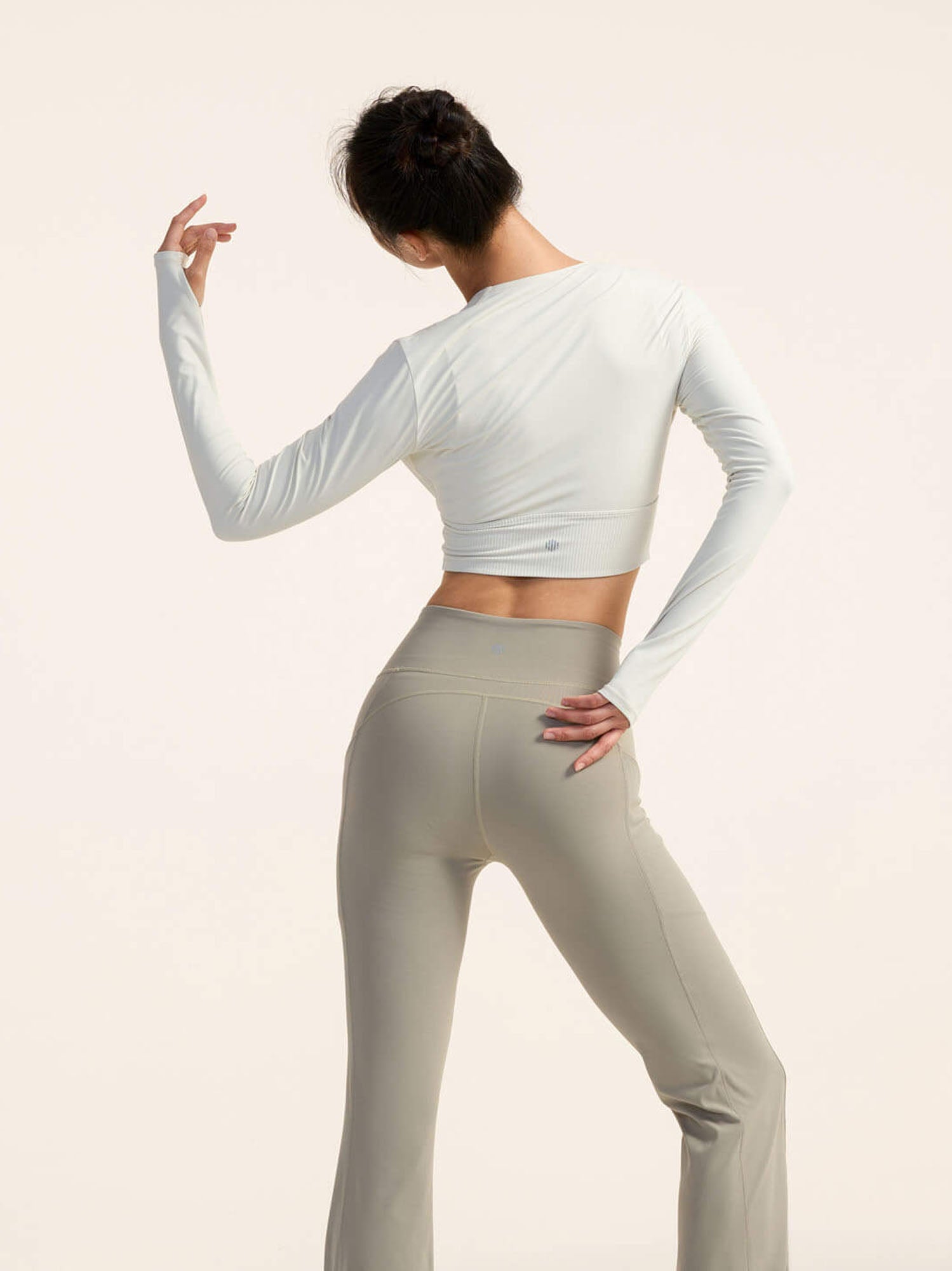 Back view of model in a white long sleeve top and beige yoga pants posing against a plain background