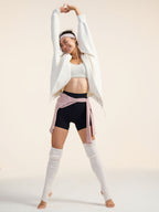 Model wearing white jacket, black shorts, and white leg warmers stretching.