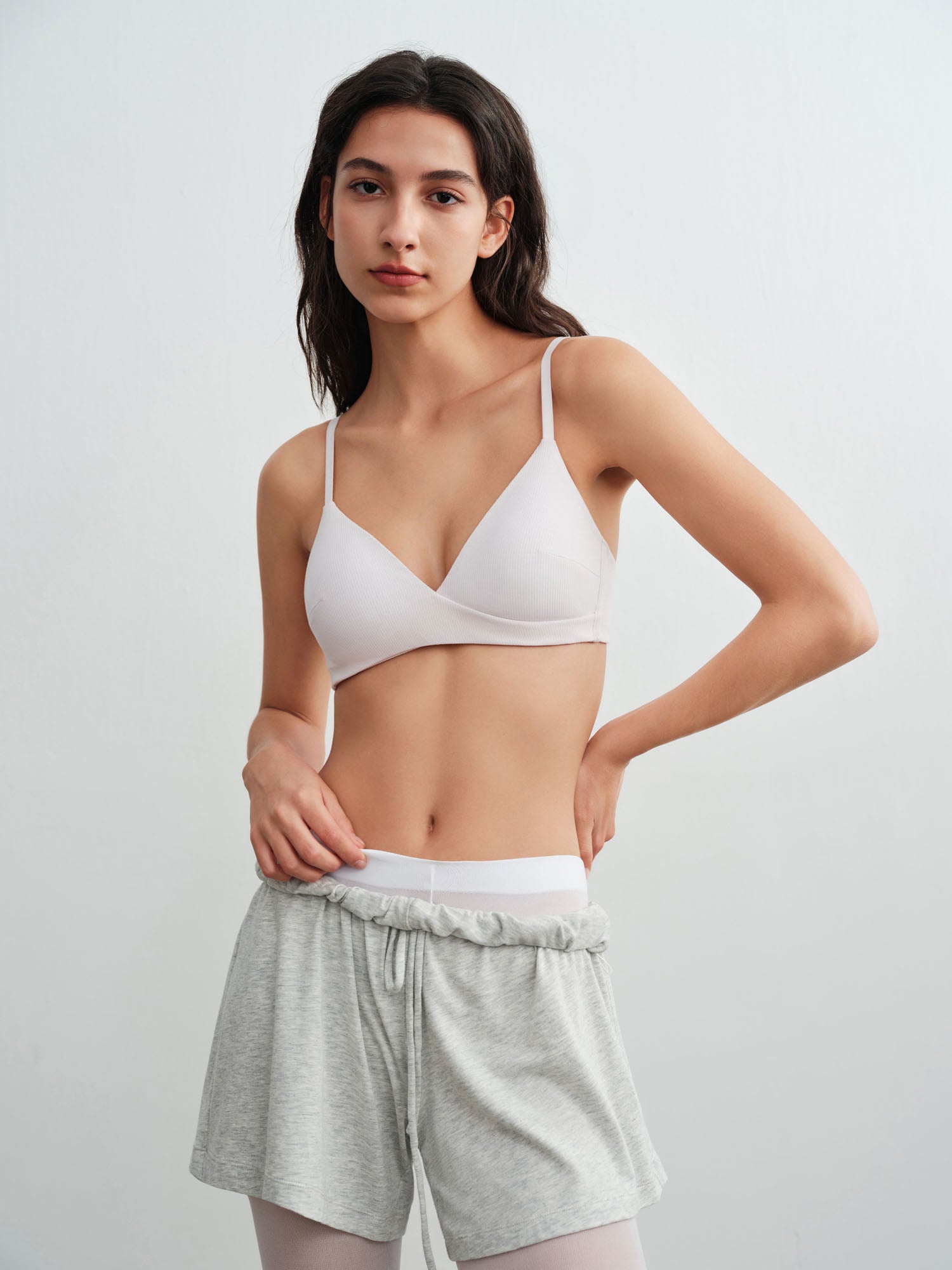 Model wearing a white bra and gray shorts on a light gray background.