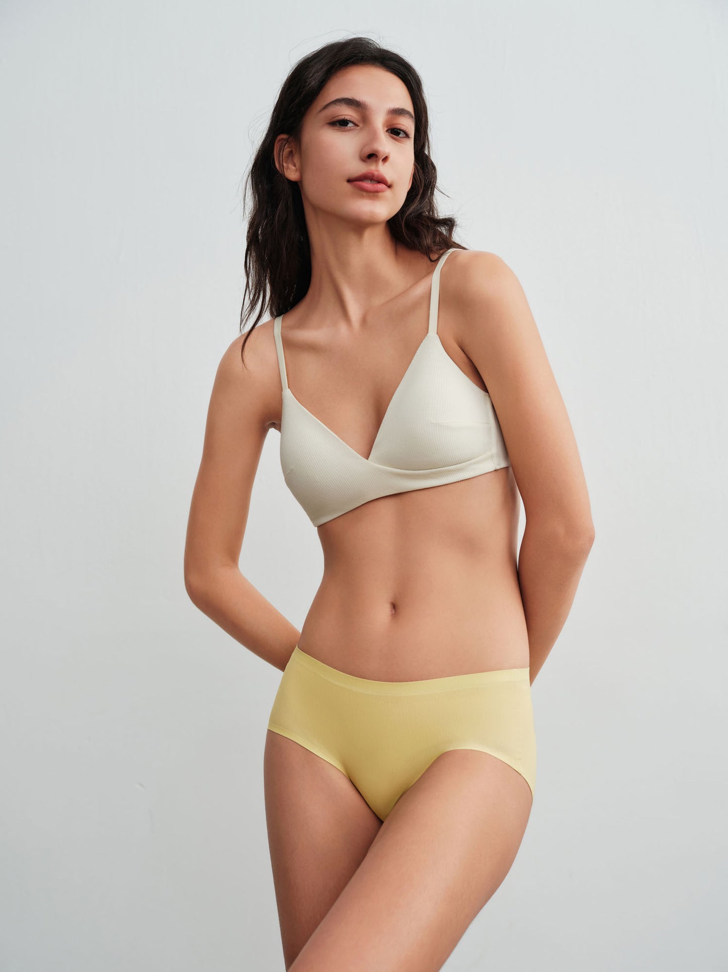 Woman wearing a white bra and green briefs against a plain background.