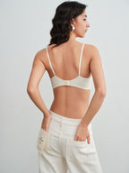 Model wearing a white bra and white pants against a plain background