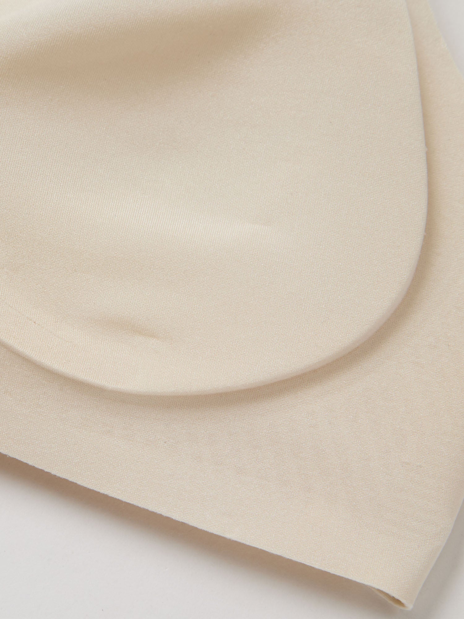 Fabric closeup of light cream bra padding on a white background
