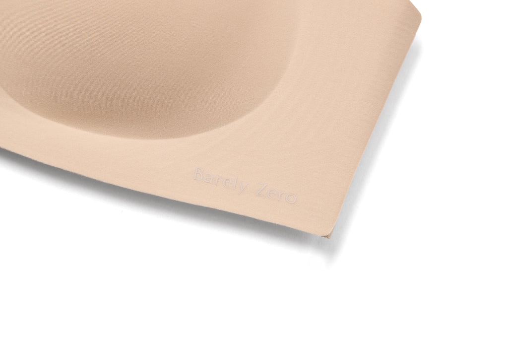 Close-up of a beige wireless bra cup with the brand name 'Barely Zero' subtly embossed on the side, set against a clean white background.