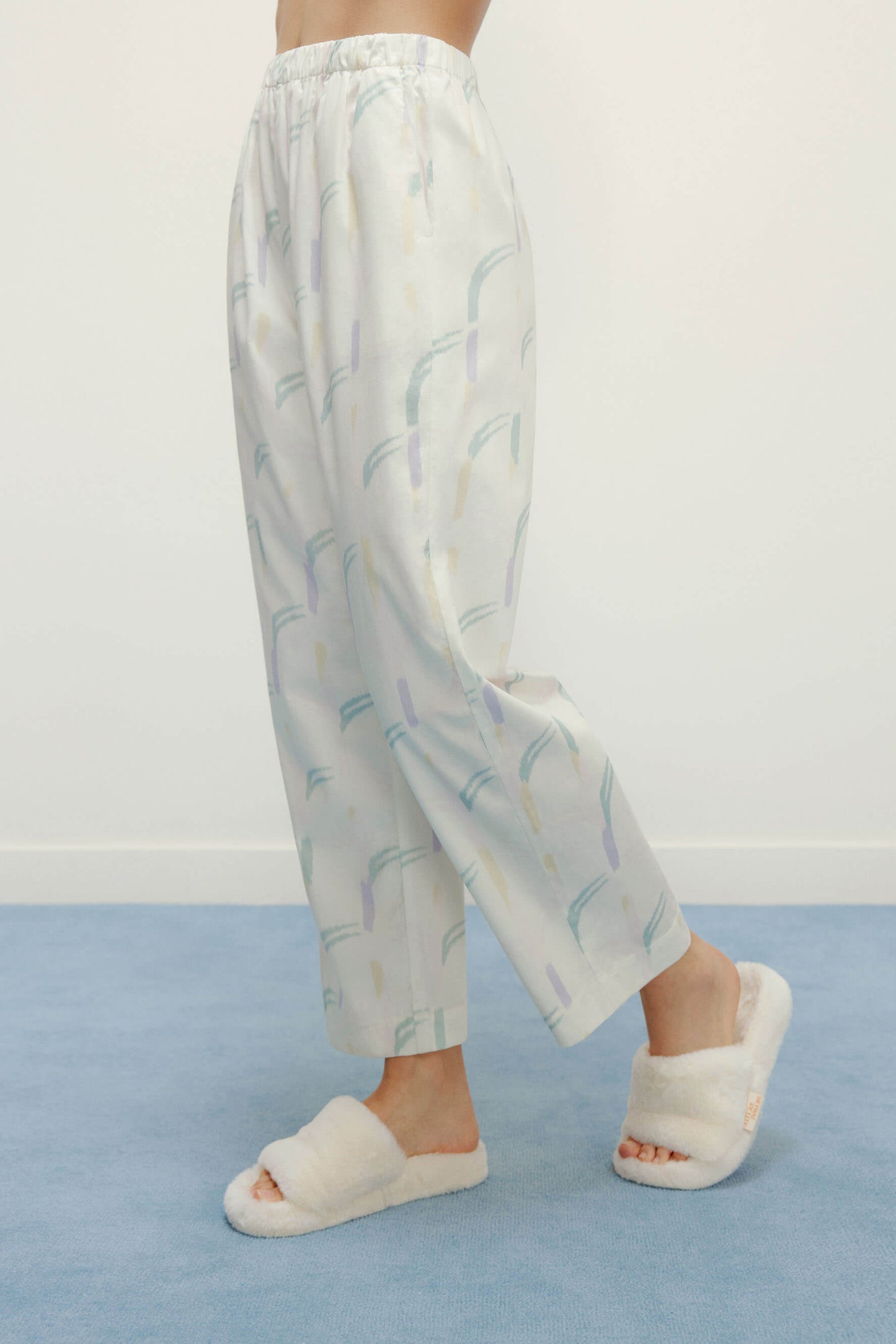 a person wearing a white pajama pants with pattern and white slippers 