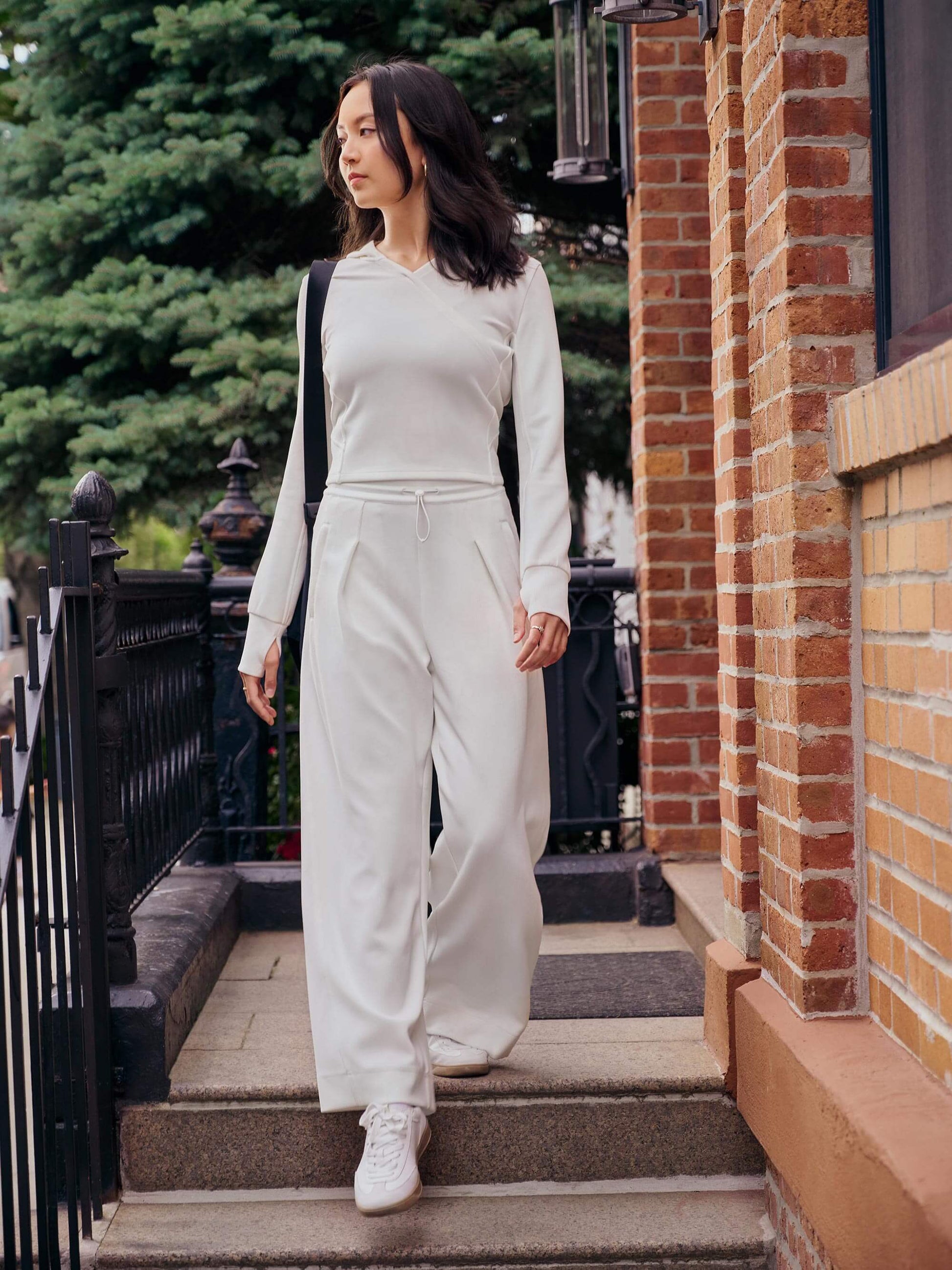 Woman wearing white sweatshirt and sweatpants with black bag over shoulders walking down stairs