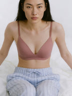 Woman wearing a mauve bralette and light blue pants on a white background