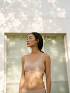 Model wearing a beige bra and briefs outdoors with a neutral background