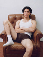 Male model in white tank top and  brief sitting in leather armchair. Trunk color.