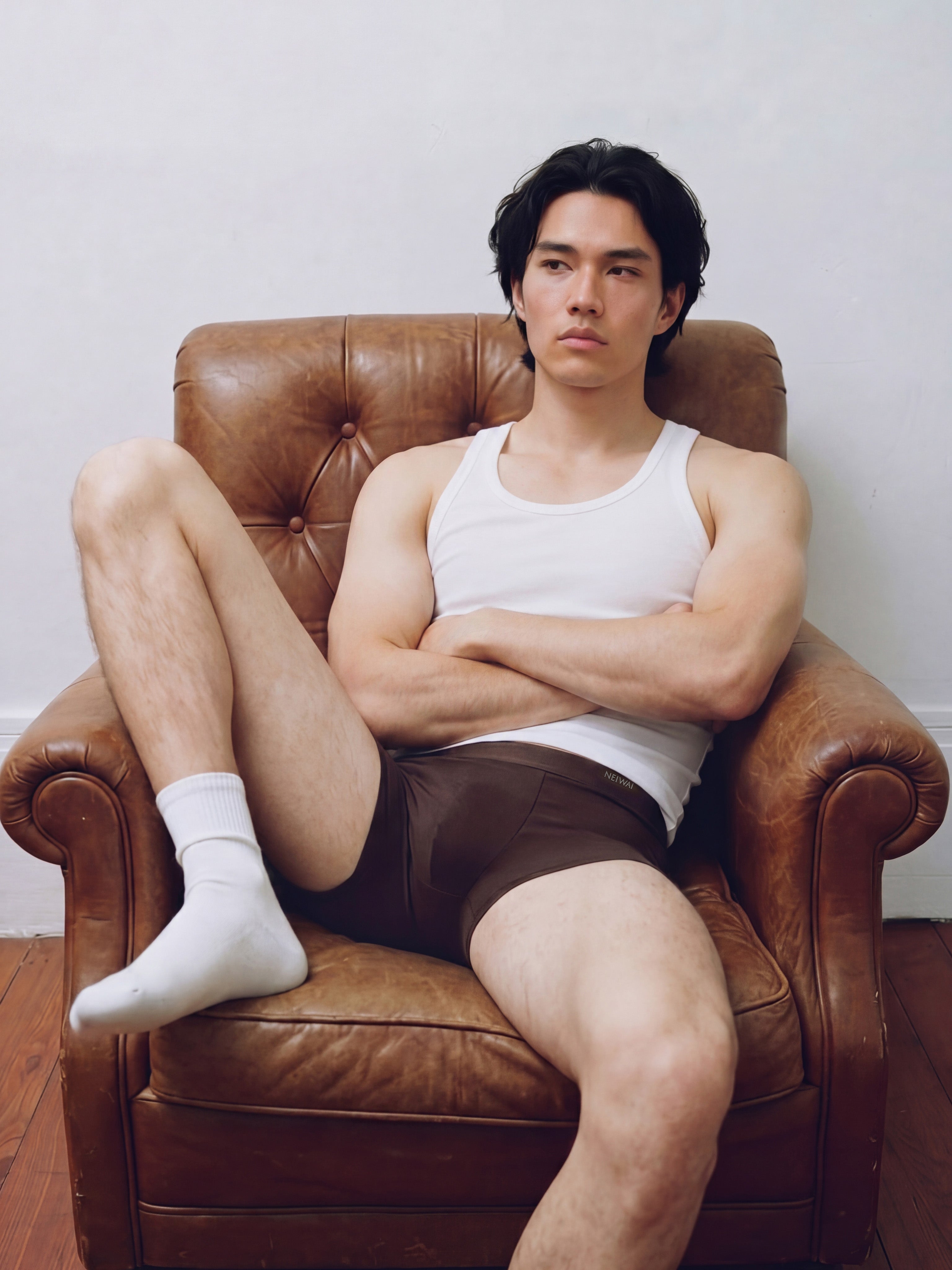 Male model in white tank top and  brief sitting in leather armchair. Trunk color.
