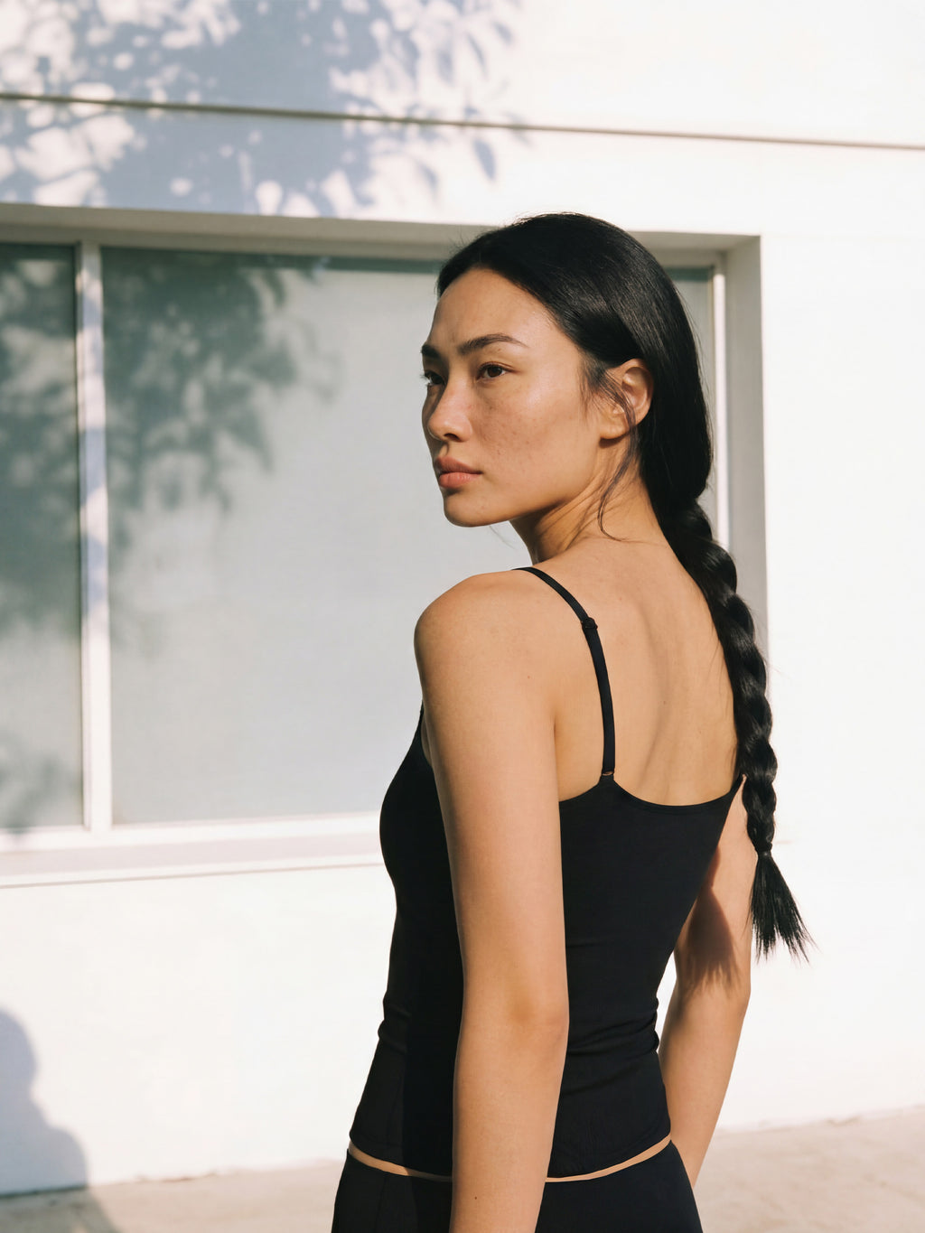 Woman with a braid wearing a black tank top standing in front of a white wall.