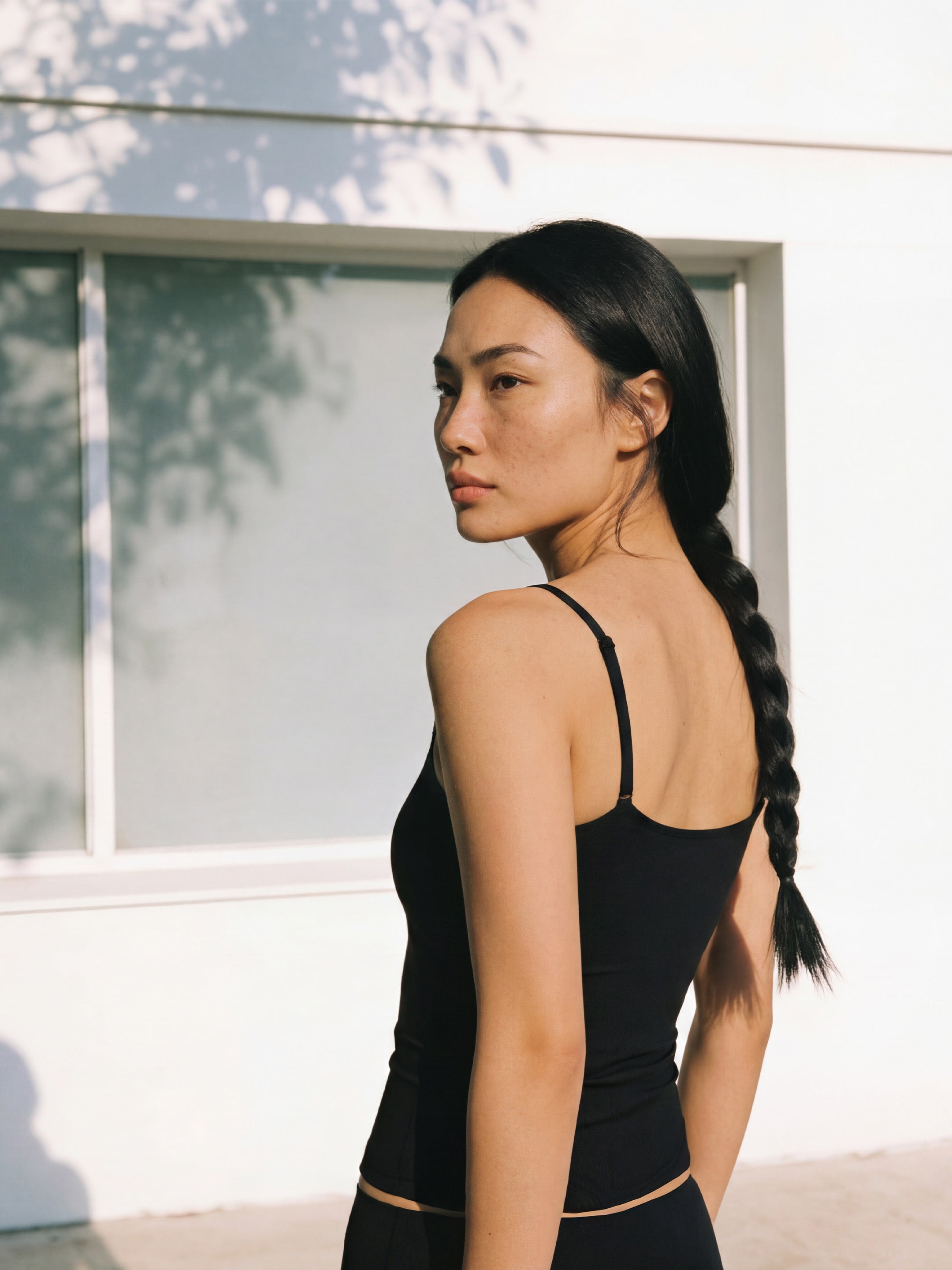 Woman with a braid wearing a black tank top standing in front of a white wall.