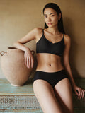 Woman wearing a black bra sitting against a beige wall with a large vase.