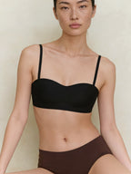 Woman wearing a black bra and brown underwear against a neutral background.  Black color. 