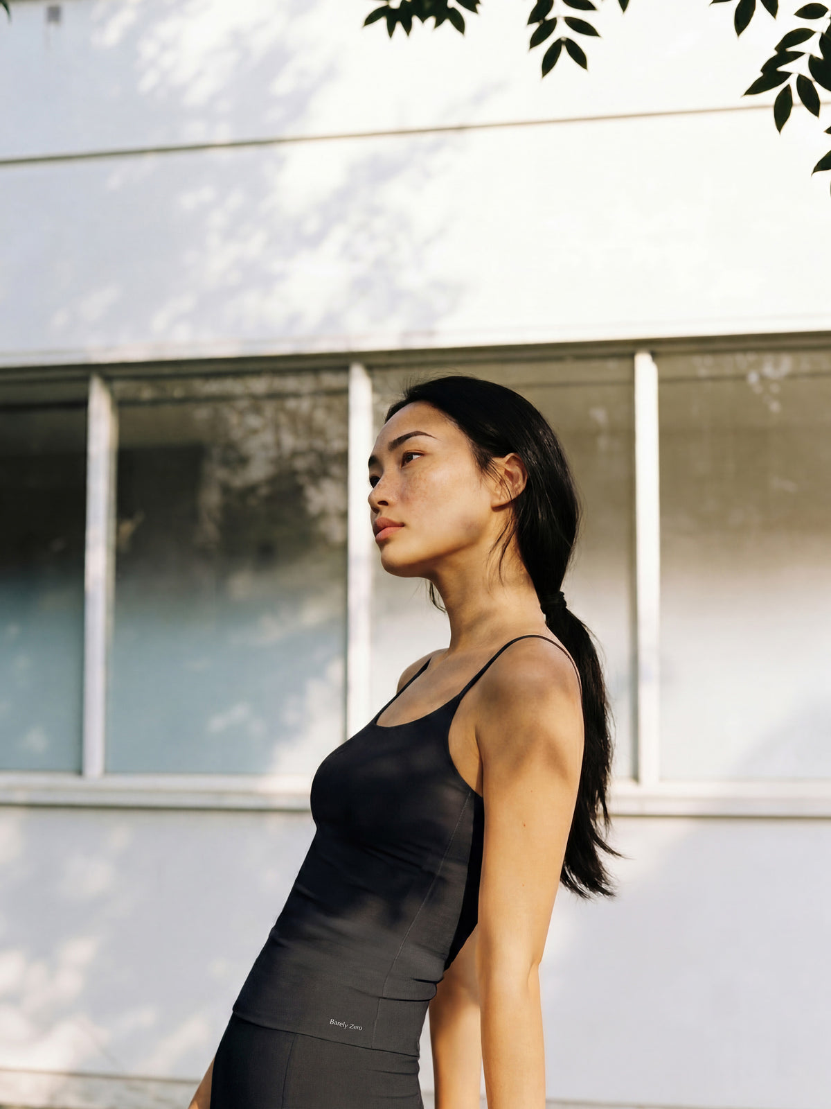 Woman in a black tank top standing outdoors with a building in the background. Black color.
