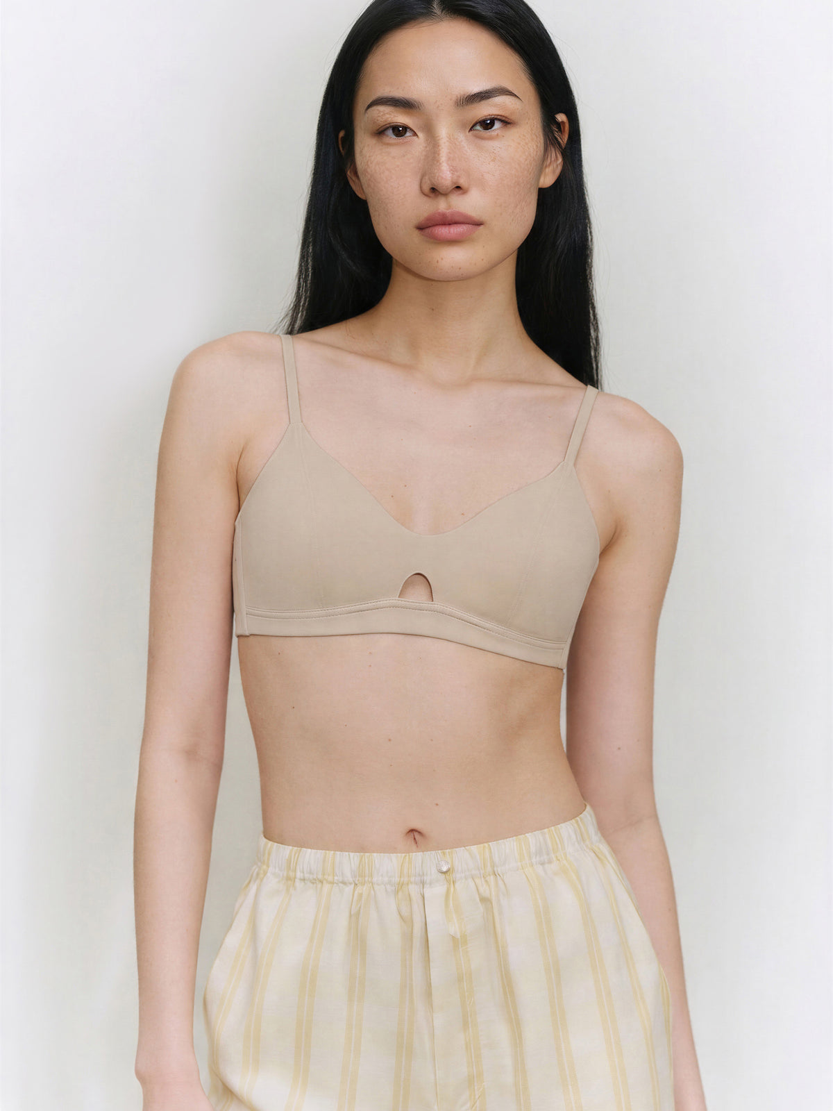 Woman wearing a beige bralette against a plain background