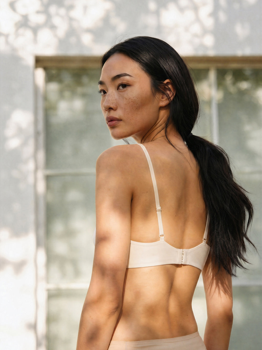 Woman wearing a beige bralette with a blurred outdoor background