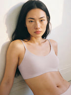 Woman wearing a light pink sports bra against a white background. Lilac Ash color.