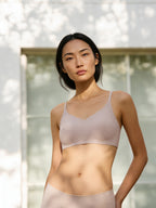 Model wearing a light mauve bra and brief set outdoors with a blurred natural background