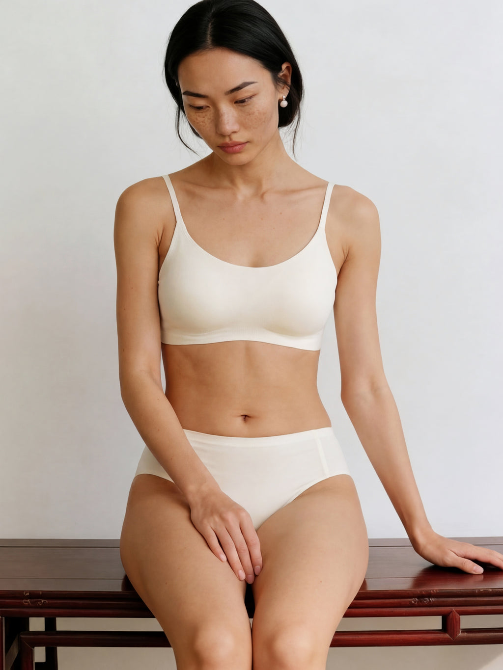 Woman wearing a white bra and panties set sitting on a wooden bench. Eggwhite color. 