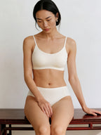 Woman wearing a white bra and panties set sitting on a wooden bench. Eggwhite color. 