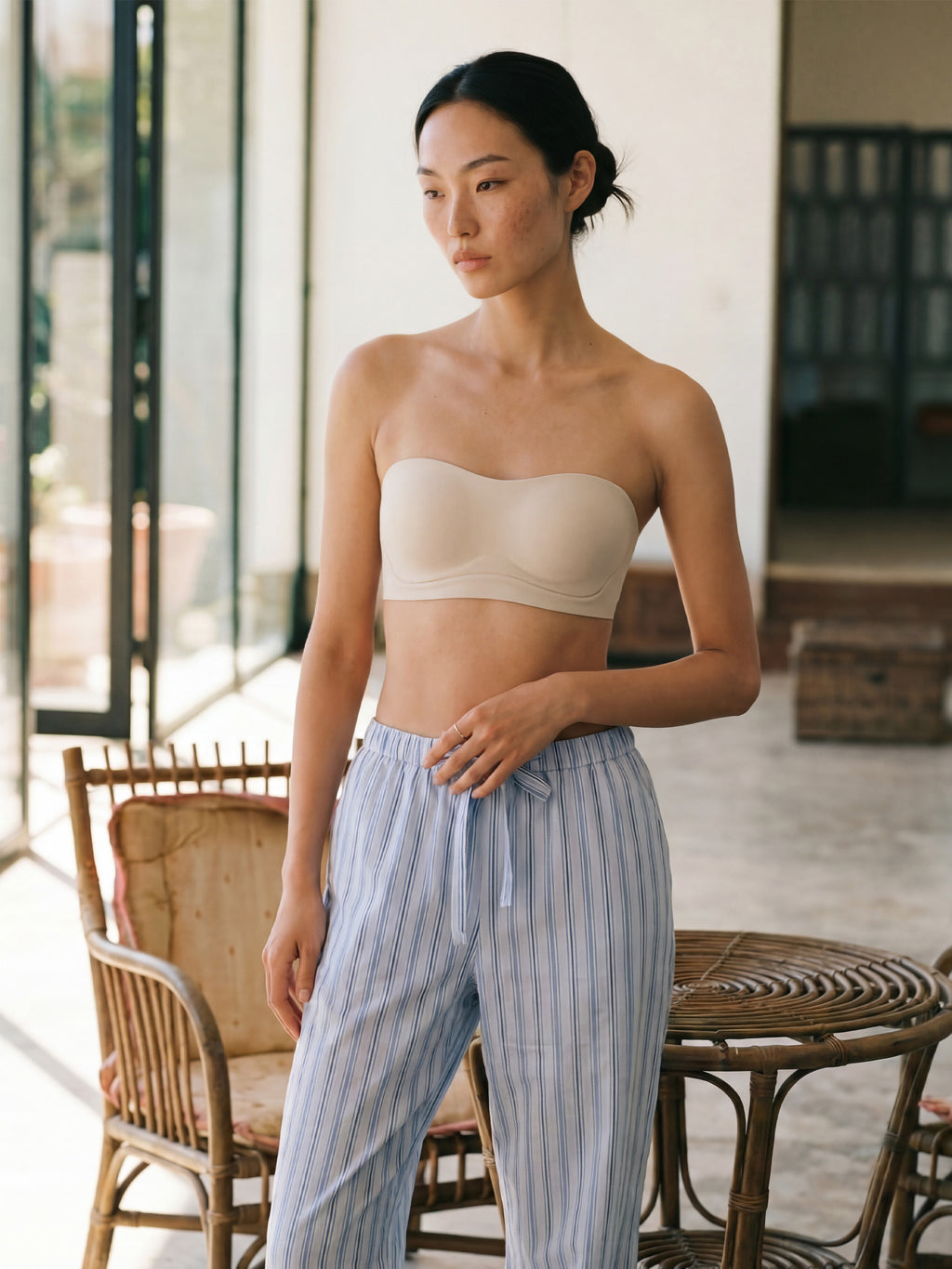 Woman wearing a beige strapless top and striped pants in an outdoor setting. Eggwhite color.