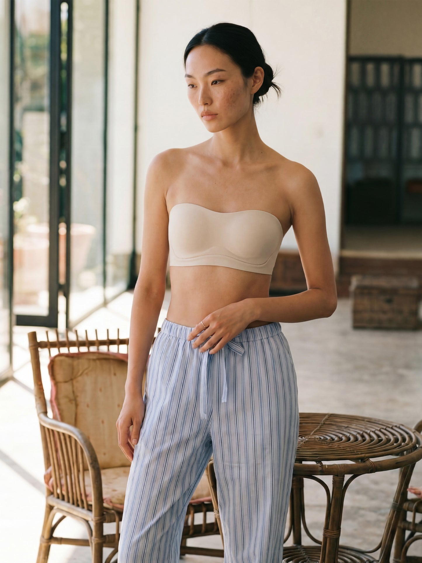 Woman wearing a beige strapless top and striped pants in an outdoor setting.