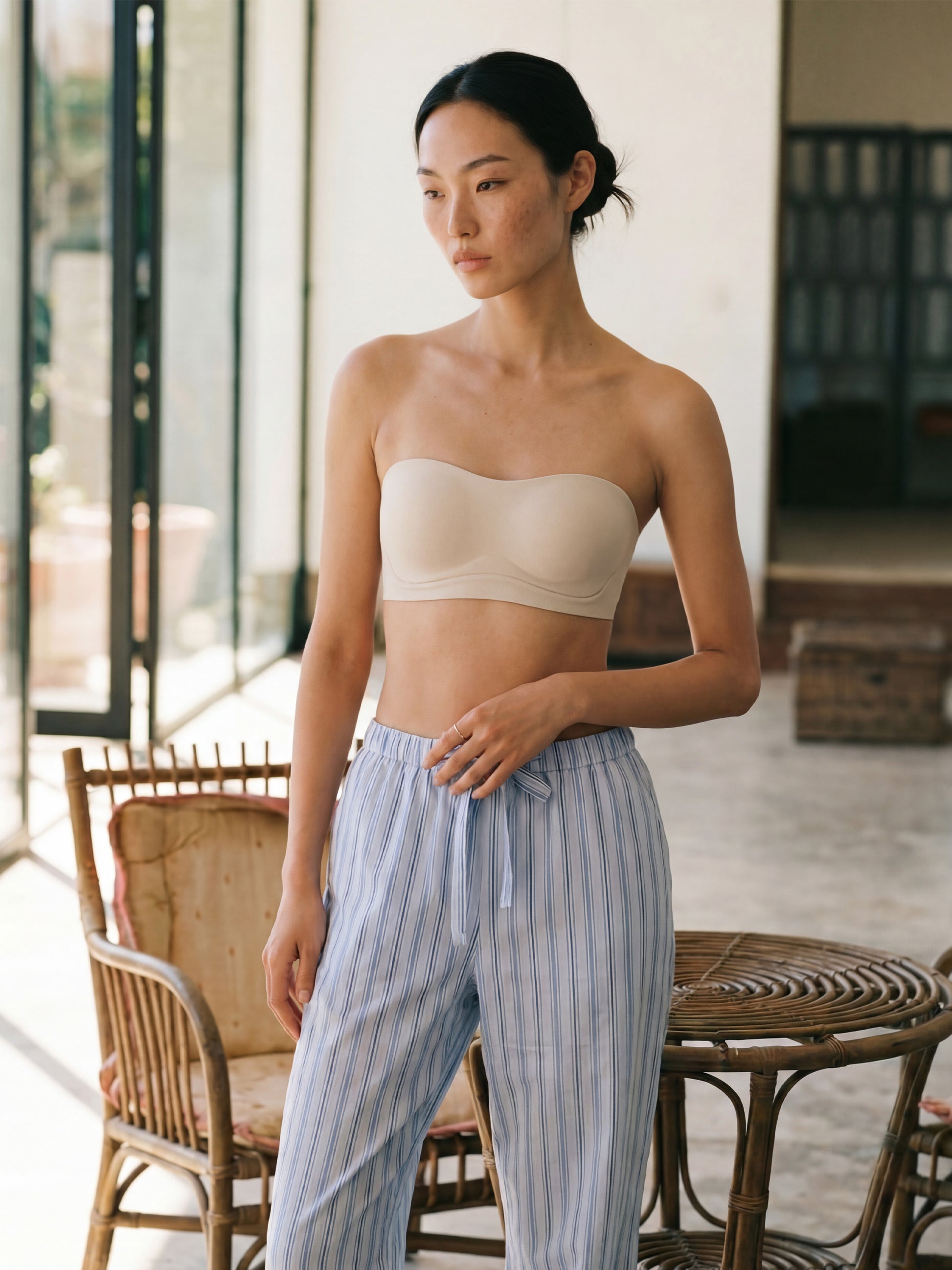 Woman wearing a beige strapless top and striped pants in an outdoor setting.