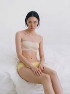 Woman wearing a beige strapless top and yellow underwear on a white background. Eggwhite color.