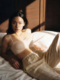 Woman in a white bra and beige pants lying on a bed with soft lighting. Eggwhite color.