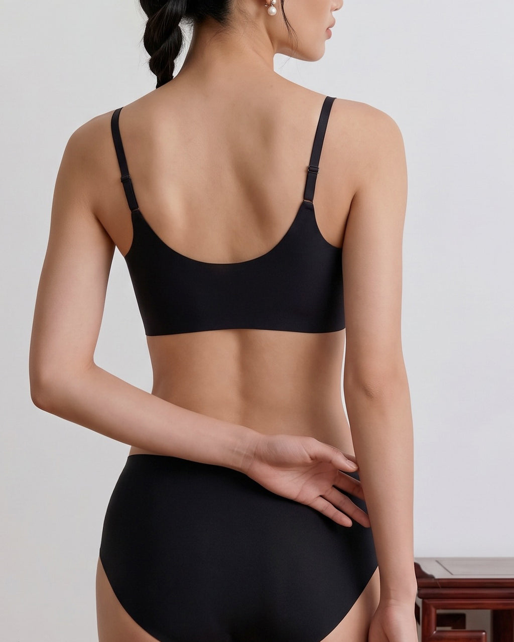 A woman shown from the back wearing a black bra and matching high-waisted briefs against a light gray indoor background. black