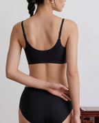A woman shown from the back wearing a black bra and matching high-waisted briefs against a light gray indoor background. black