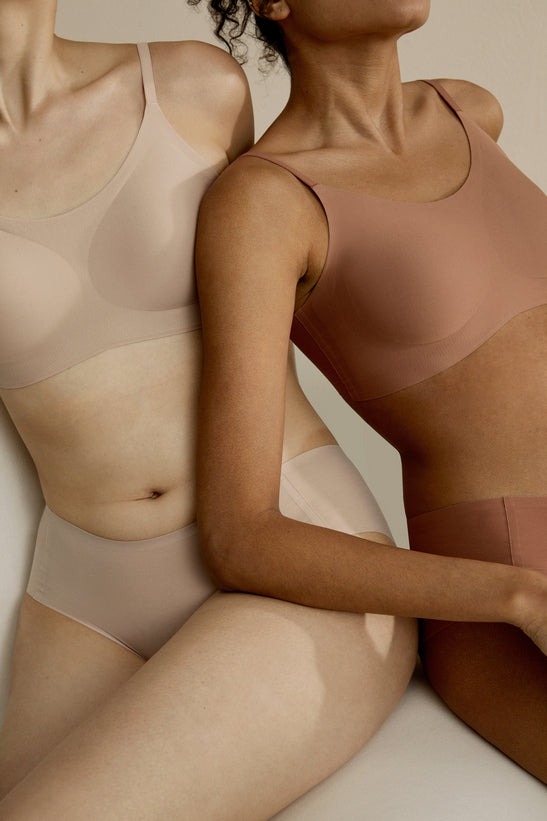 two women in bra and brief, one in beige and one in rust color