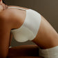 Seated woman bending over wearing spaghetti strap pullover bra in off-white and matching underwear