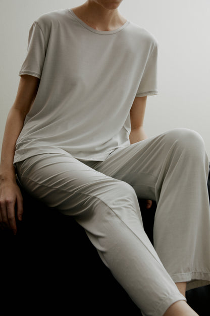 Woman sitting wearing light gray short sleeve pajama shirt and matching pants