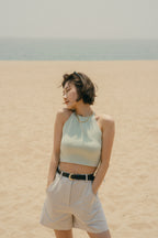 Woman standing on beach wearing light green colored tank top with belted shorts
