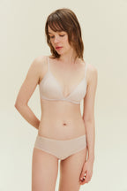Front view of model wearing light pink bra with matching briefs and putting her hand behind her back.