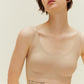 A young woman wearing a Barely Zero Classic Bra Trio in beige, embossed with the phrase "my body is a cage set my spirit free," stands against a light beige background, looking directly at