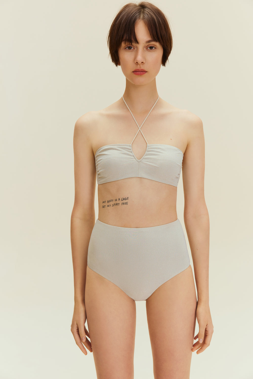 Woman standing wearing gold halter neck bikini bop and high waisted bikini bottom