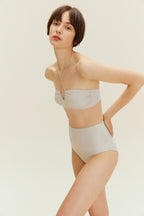 Woman standing leaning forward wearing gold halter neck bikini bop and high waisted bikini bottom
