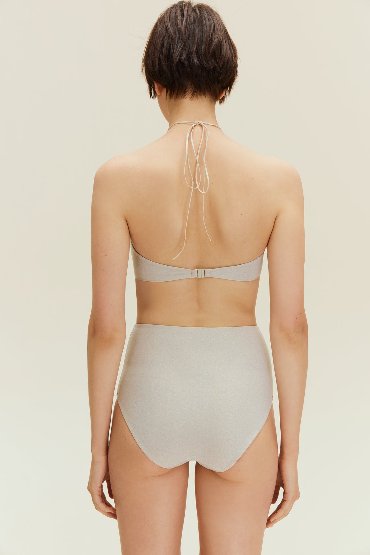 Back view of woman standing wearing gold halter neck bikini bop and high waisted bikini bottom