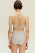 Back view of woman standing wearing gold halter neck bikini bop and high waisted bikini bottom