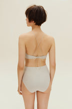 Back view of woman standing wearing gold halter neck bikini bop and high waisted bikini bottom