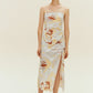 Woman standing wearing spaghetti strap dress with brown, beige, white print with high slit on side