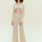 Woman standing wearing off white knit pants with bikini top and off white knit cardigan